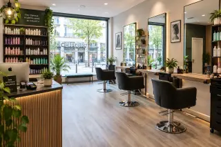 Salon de coiffure moderne et vide, intérieur lumineux avec baies vitrées, fauteuils alignés, comptoir d'accueil, mobilier et produits capillaires bien rangés.